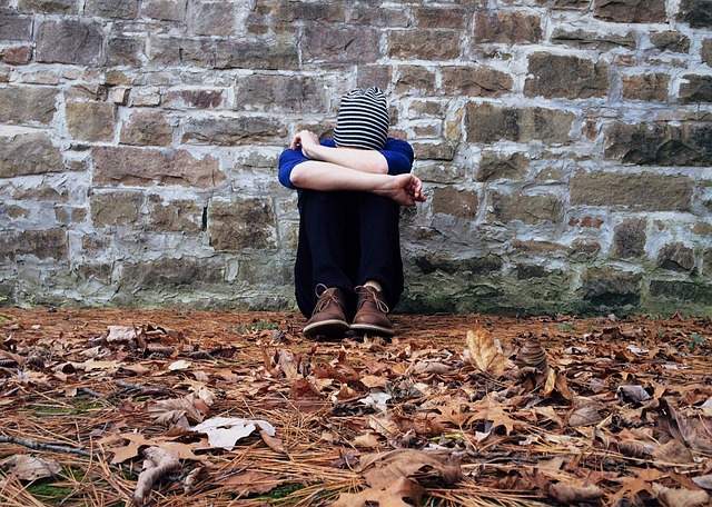 personne triste assise par terre contre le mur tenant sa tête entre ses mains