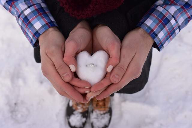 mains d'un couple tenant une bague de fiançailles dans la neige