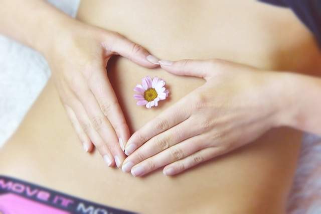 ventre de femme avec une fleur et les mains en cœur