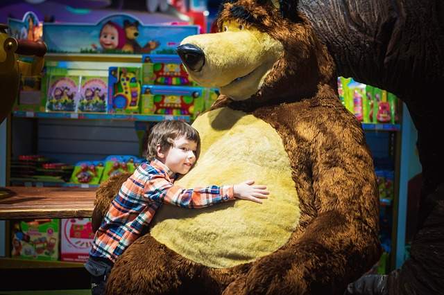 enfant dans sa chambre qui tient un gros ours en peluche dans ses bras