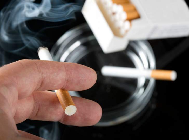 main tenant une cigarette allumée, cendrier et paquet de cigarettes