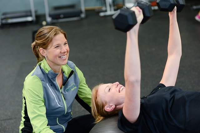 fille qui soulève des haltères et son coach sportif