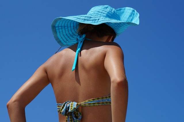 femme de dos en maillot de bain avec un chapeau sous le soleil