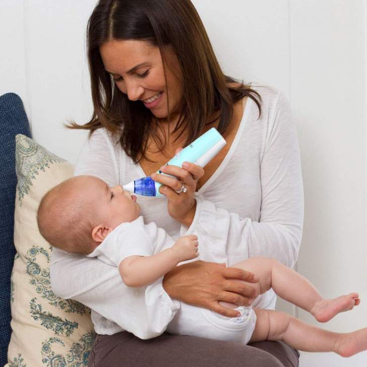 Bébé dans les bras de sa maman qui est entrain de lui déboucher le nez avec un mouche-bébé électrique