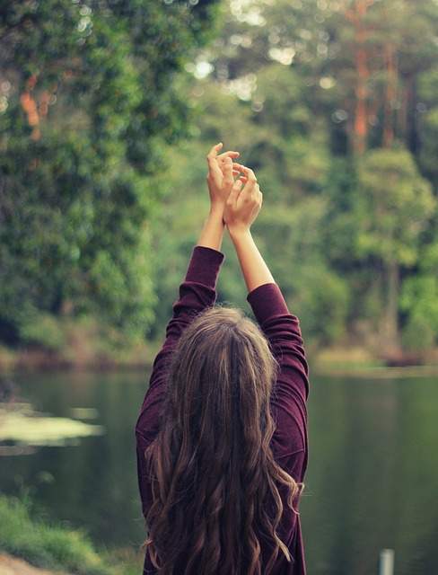 femme de dos qui fait des étirements devant un lac dans une forêt