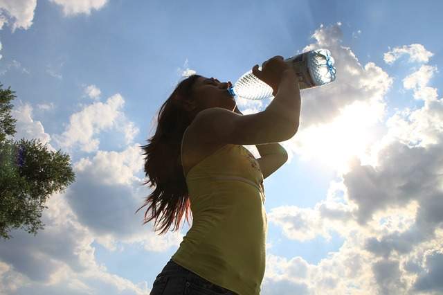 femme qui bois de l'eau à la bouteille sous un ciel bleu