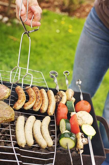 barbecue dans l'herbe avec une main tenant une pince pour barbecue pour retourner les saucisses et les légumes