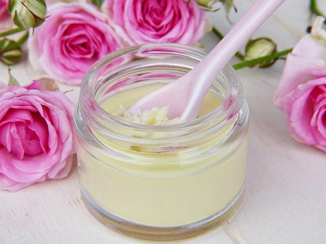 pot de crème de beauté avec une petite cuillère en porcelaine entouré de roses fraîches