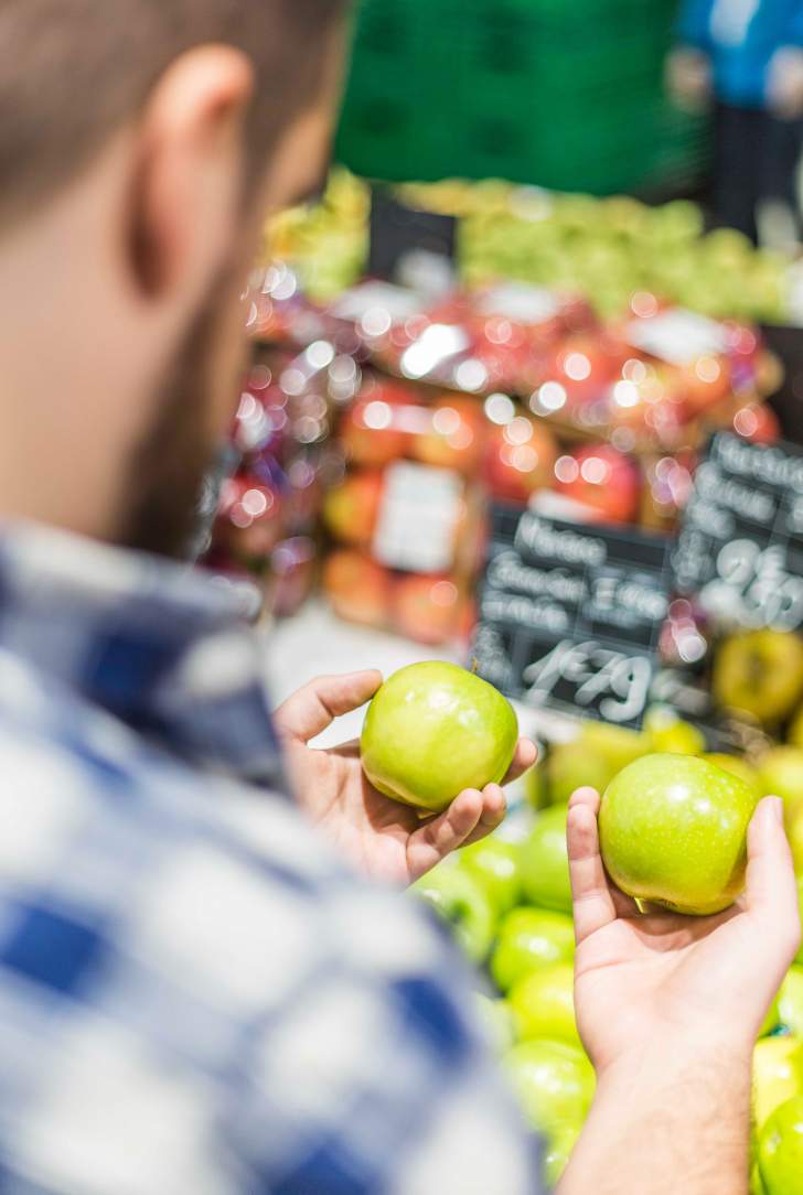 homme devant un étalage de fruits et légumes entrain de choisir des pommes