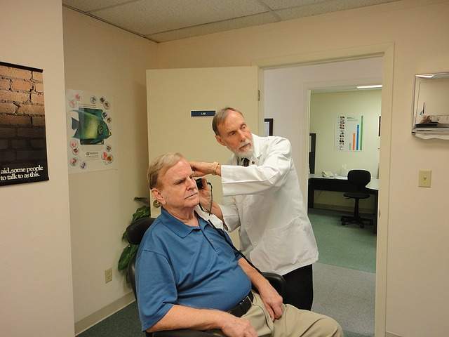 patient assis se faisant ausculter l'oreille par un médecin ORL