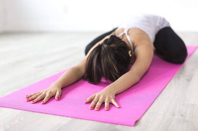 femme faisant du yoga sur un tapis de yoga rose