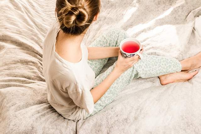 femme en pyjama assise sur un lit tenant une tisane 