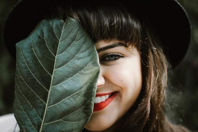 femme souriante avec le visage à moitié recouvert par une grande feuille d'arbre