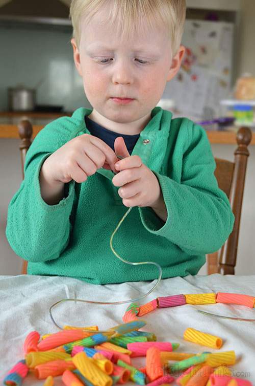 enfant en train d’enfiler les pâtes