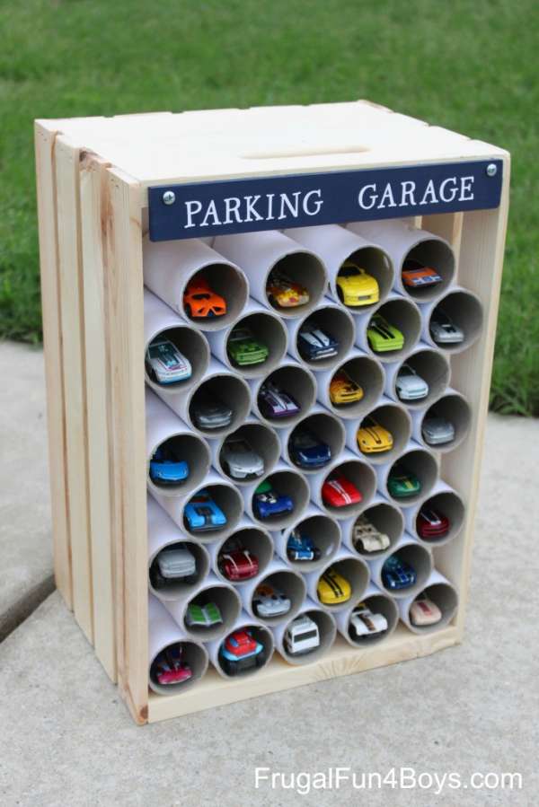 Un parking-présentoir pour les voitures miniatures des enfants avec une caisse en bois et des tubes pour envoi postal en carton