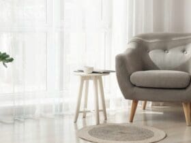 un fauteuil et un table d'appoint devant des rideaux voilage blanc