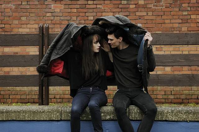 couple assis qui se protège de la pluie avec leurs vestes