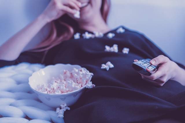 femme tenant une télécommande et mangeant du pop-corn