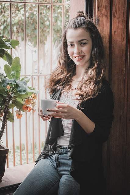 femme souriante prêt de la fenêtre tenant une tasse de café