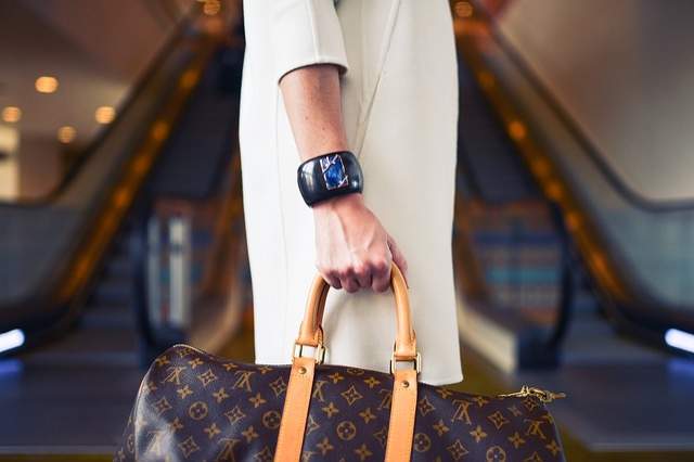 femme avec un manteau blanc un gros bracelet et un sac Louis Vuitton