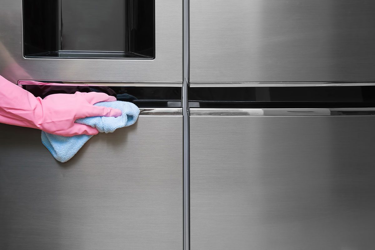 Main gantée nettoyant une porte de frigo en inox