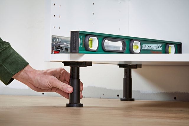 Une personne ajuste la hauteur d'un pied de meuble de cuisine avec un niveau à bulle posé dessus.