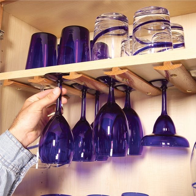Plusieurs rangées de verres à pied suspendus sous un placard de cuisine grâce à des moulures en T.