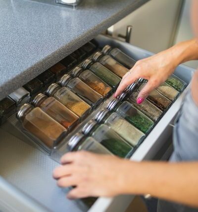 Une main d'une femme en train de ranger les boîtes à épices dans un tiroir de cuisine