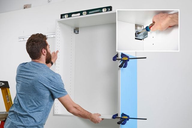 Une personne installe un meuble de cuisine haut sur son rail.