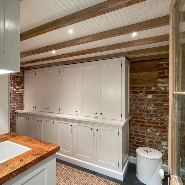 Une buanderie avec un mur en briques, des poutres en bois apparentes et du lambris blanc entre les poutres.