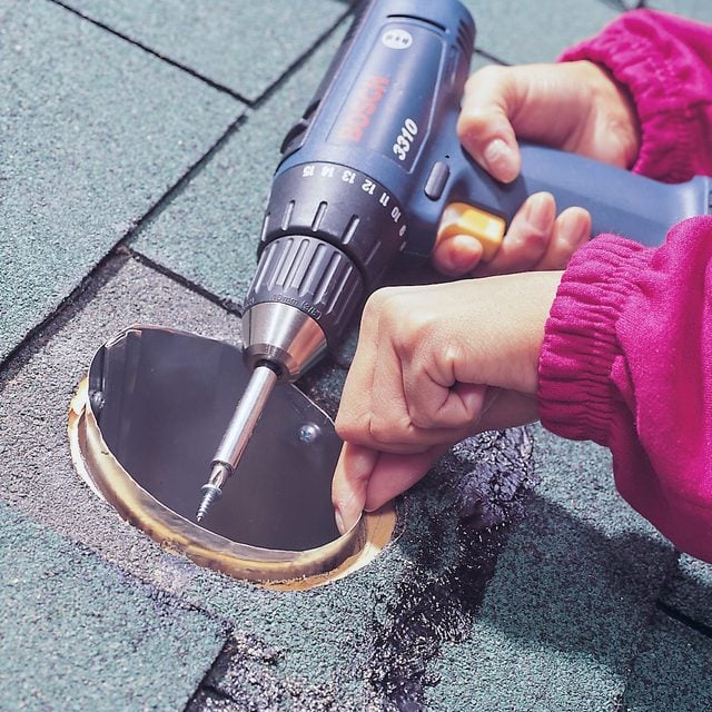 Une main tenant une scie sabre découpe un trou circulaire dans un toit en bardeaux.