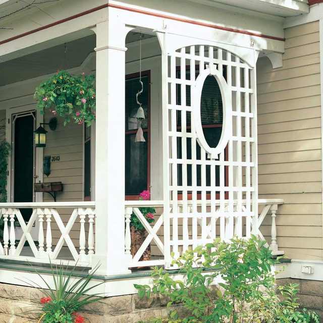 Un treillis blanc avec une découpe ovale se dresse à côté d'un porche.