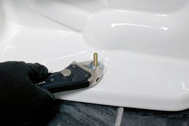 Personne resserrant l'écrou à la base d'un WC avec une clé.