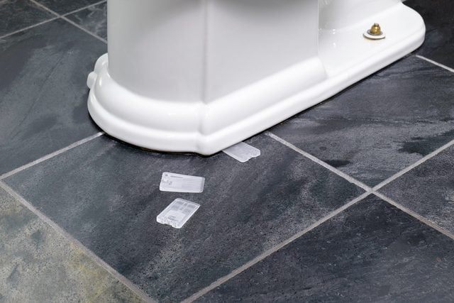 Main insérant une cale en plastique sous la base de toilettes pour les stabiliser.