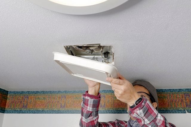 Une personne vérifiant l'absence de courant avec un testeur électrique sur les fils du ventilateur de salle de bain.