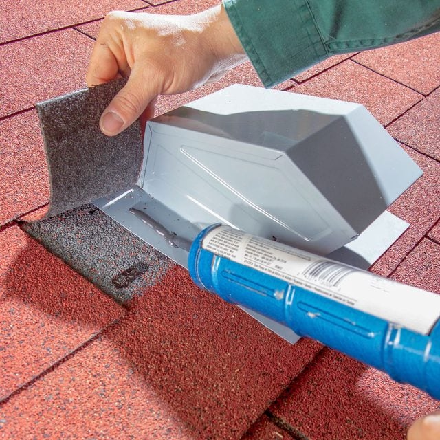 Une main applique du mastic de toiture autour d'un chapeau de ventilation fraîchement installé.