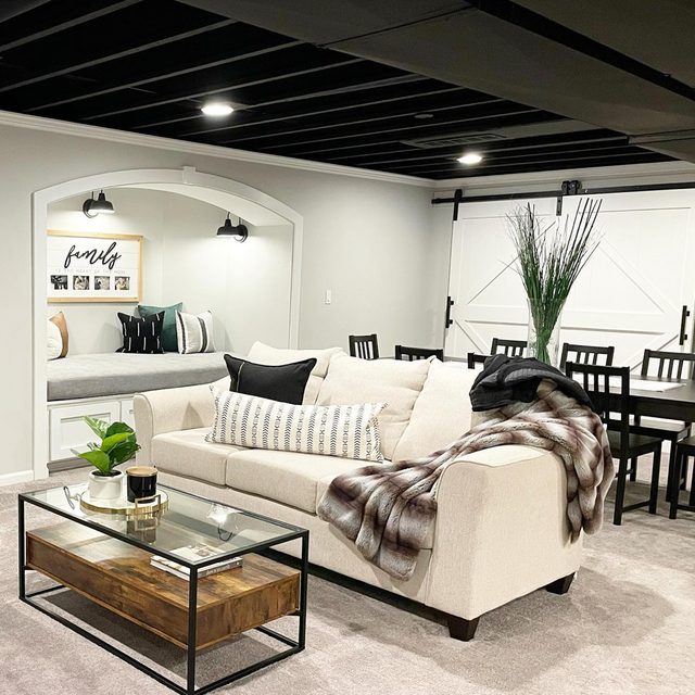 Un salon de sous-sol moderne avec un plafond brut peint en noir et des spots intégrés.