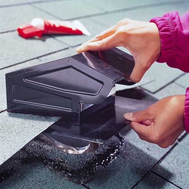 Une personne positionne la base d'un chapeau de toiture sous des tuiles soulevées.