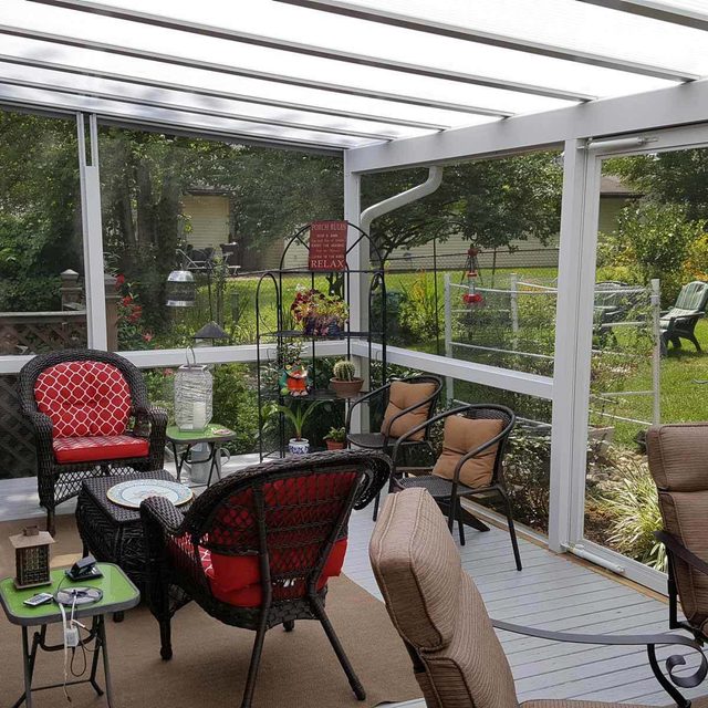 Une véranda ensoleillée avec des meubles en osier et des coussins rouges.