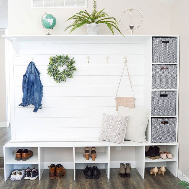 Un meuble d'entrée fait maison, peint en blanc, avec un banc, des crochets et des rangements pour les chaussures.