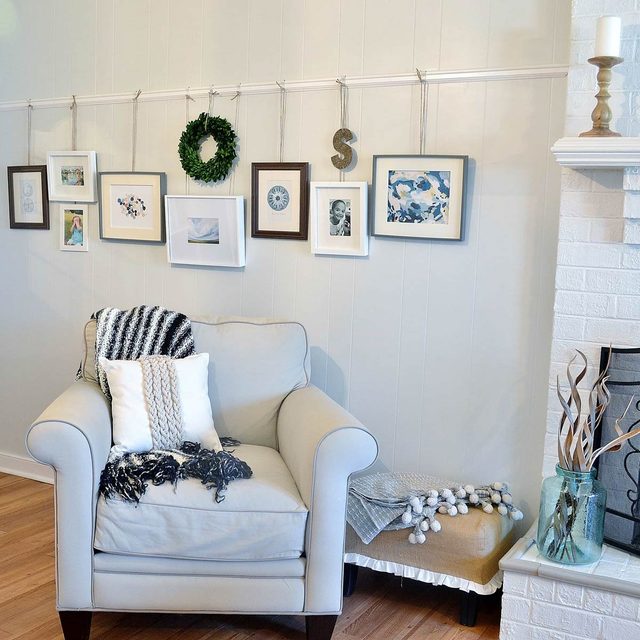 Un mur décoré avec des cadres et une couronne accrochés à une cimaise, au-dessus d'un fauteuil.