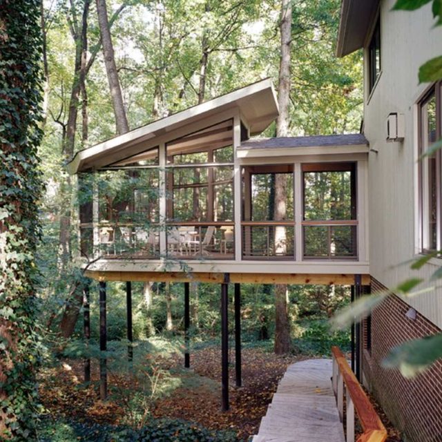 Une maison moderne sur pilotis avec de grandes fenêtres et une terrasse, entourée d'arbres.