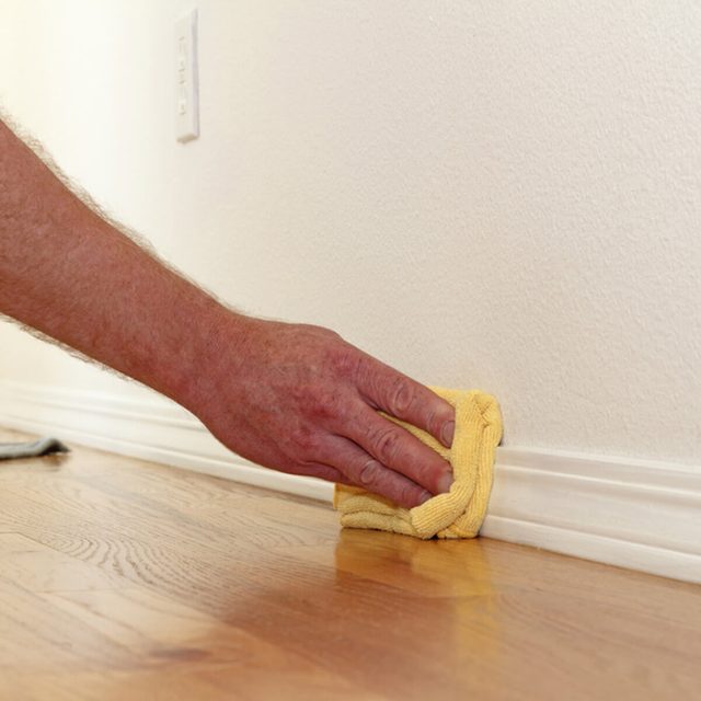 Une main nettoyant une plinthe blanche classique le long d'un parquet.