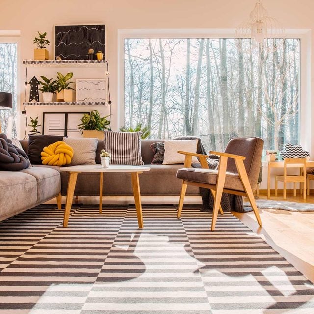 Un salon lumineux avec un canapé gris garni de coussins variés, dont un jaune en forme de nœud.