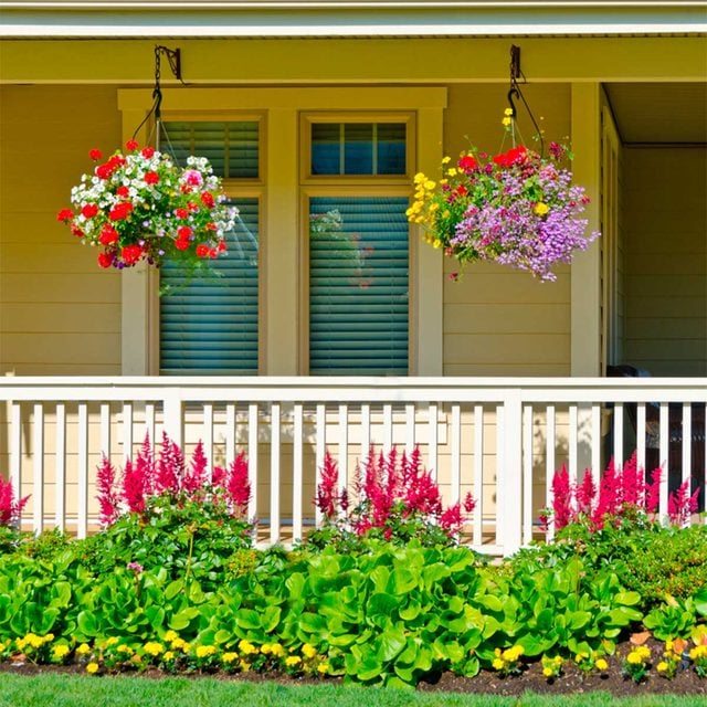 Paniers de fleurs suspendus au-dessus d'une balustrade blanche, avec des fleurs de jardin colorées en dessous.
