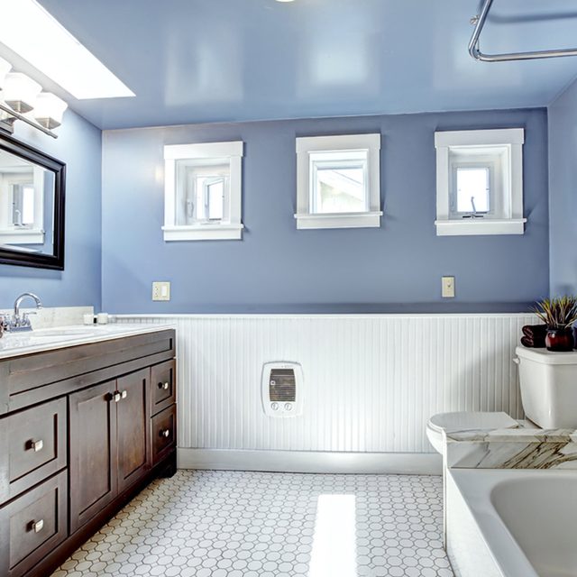 Une salle de bain avec un mur bleu, des boiseries basses peintes en blanc et des fenêtres.
