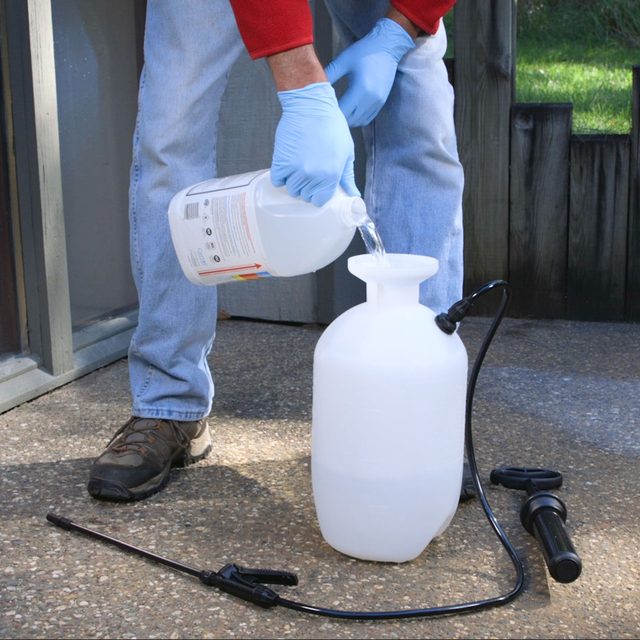 Une personne portant des gants verse un liquide d'un bidon dans un pulvérisateur de jardin.