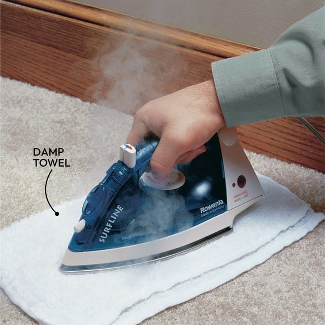 Personne utilisant un fer à repasser et un chiffon pour transférer la cire d'un tapis vers le chiffon.