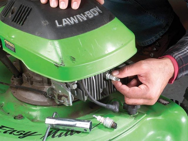 Une personne nettoie le moteur d'une tondeuse.