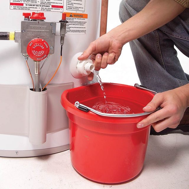 Une personne vidange un chauffe-eau dans un seau rouge.